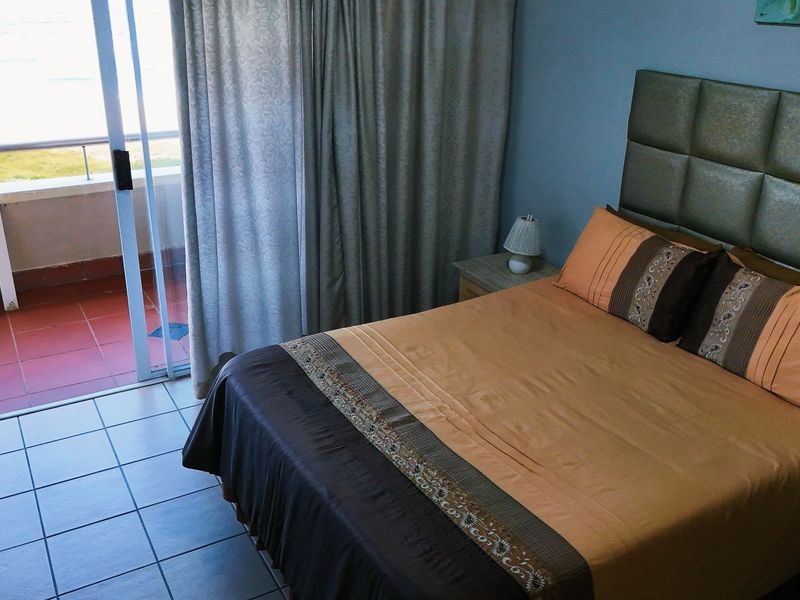 A bedroom featuring tiled flooring and a sliding glass door providing direct access to an outdoor balcony with coastal views.
