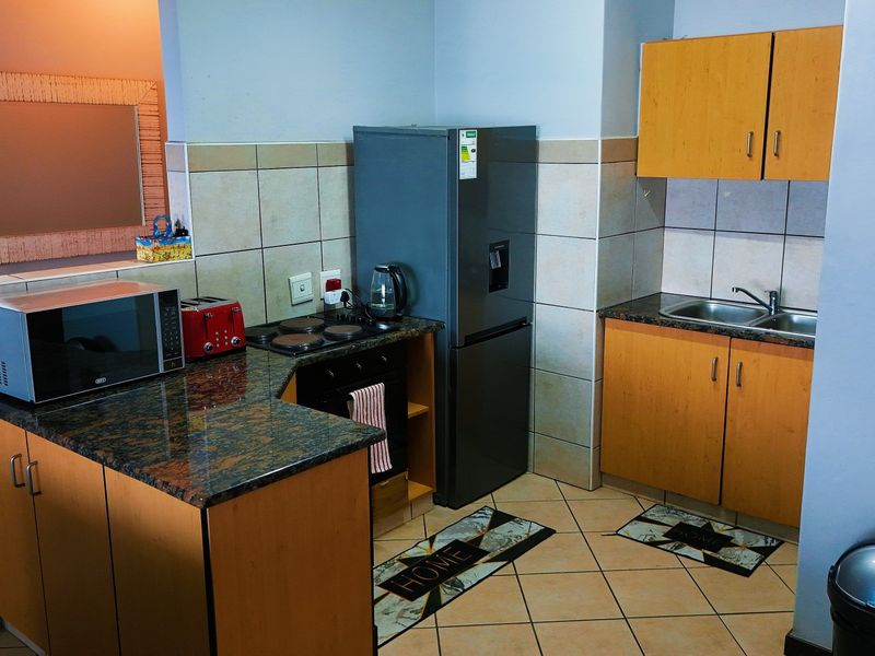 Compact kitchen featuring granite countertops, laminate cabinetry, built-in oven and hob, and tiled flooring with a functional layout.