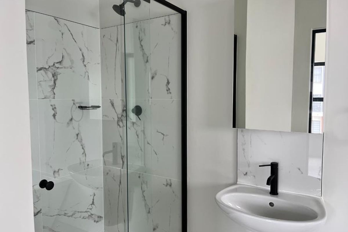 Modern bathroom featuring a walk-in shower with black-framed glass, marble-look wall tiles, a pedestal sink with a black faucet, and a wall-mounted mirror.