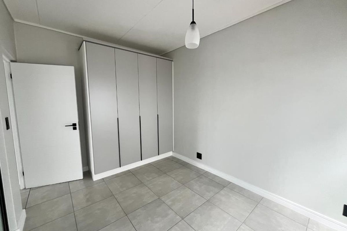 A clean, modern bedroom featuring neutral grey tones, large format floor tiles, and a sleek built-in wardrobe with minimalist hardware.