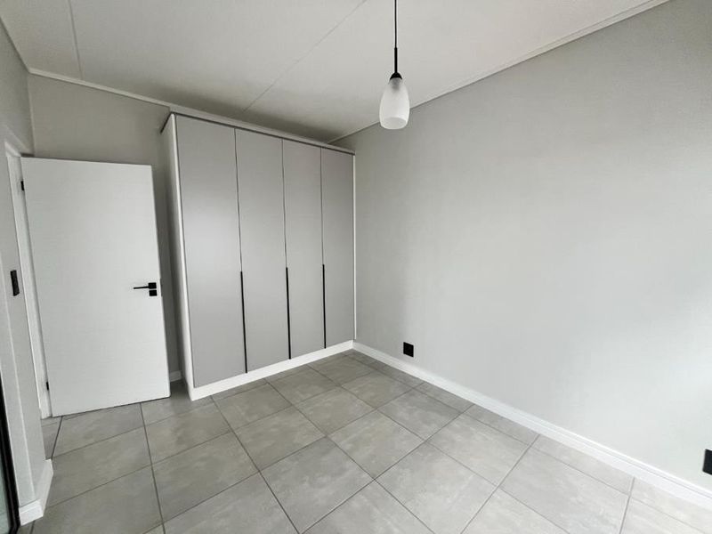 A clean, modern bedroom featuring neutral grey tones, large format floor tiles, and a sleek built-in wardrobe with minimalist hardware.
