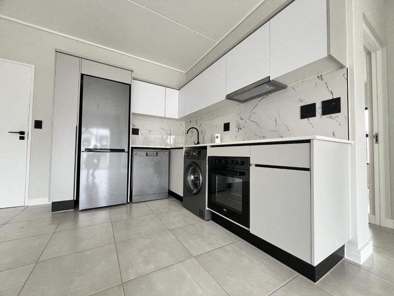 Modern kitchen featuring sleek white cabinetry, marble-look splashback, integrated oven, extractor fan, and neutral tiled flooring in a clean, contemporary layout.
