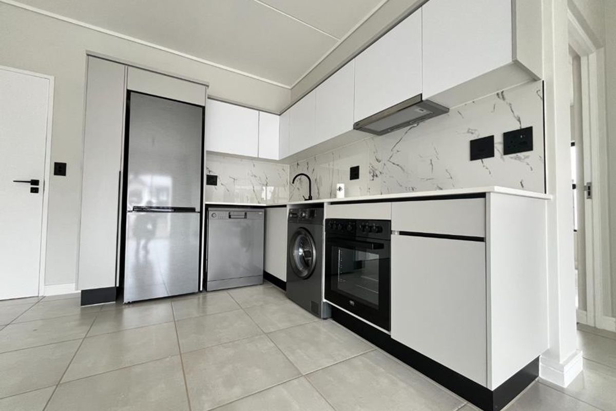 Modern kitchen featuring sleek white cabinetry, marble-look splashback, integrated oven, extractor fan, and neutral tiled flooring in a clean, contemporary layout.