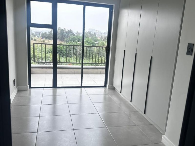 Modern bedroom featuring neutral tiled flooring, floor-to-ceiling built-in cupboards, and a sliding glass door providing access to a private balcony with scenic views.
