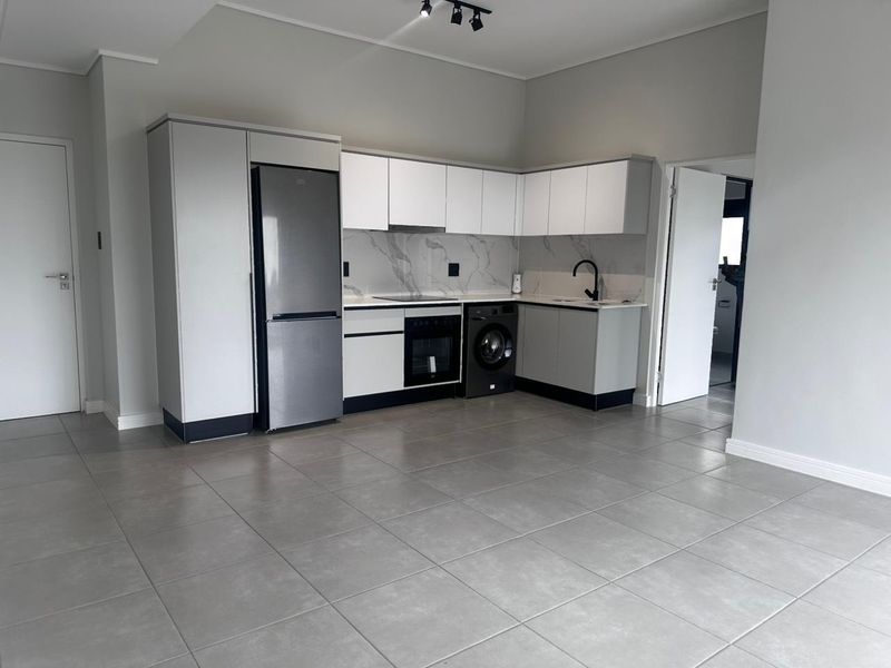 Modern open-plan kitchen featuring sleek white cabinetry, marble-look splashback, integrated appliances, and neutral floor tiles in a clean, well-maintained space.