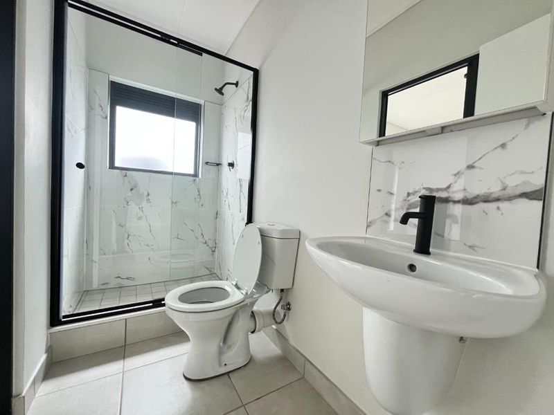 Modern bathroom featuring a walk-in shower with black frame, marble-look wall tiles, pedestal washbasin with black faucet, and a clean, contemporary aesthetic.