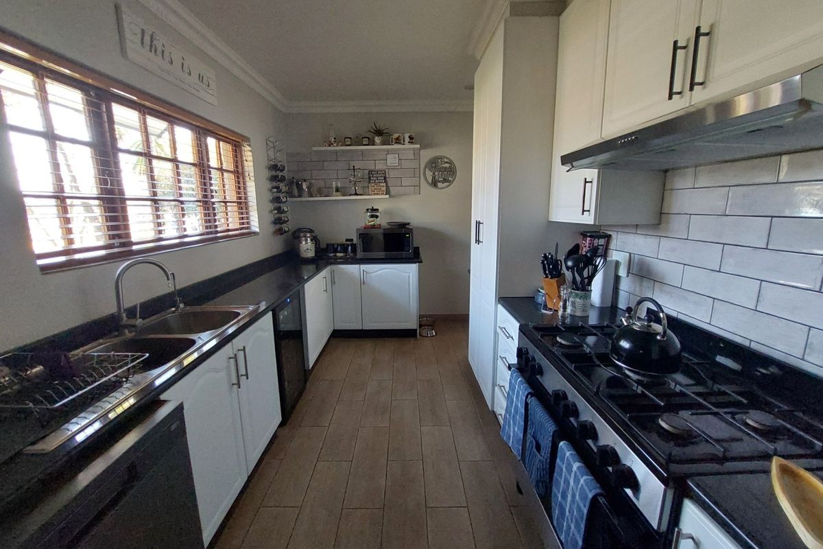 A well-maintained galley-style kitchen featuring white cabinetry, dark granite countertops, subway tile backsplash, and a gas stove with an integrated extractor fan.