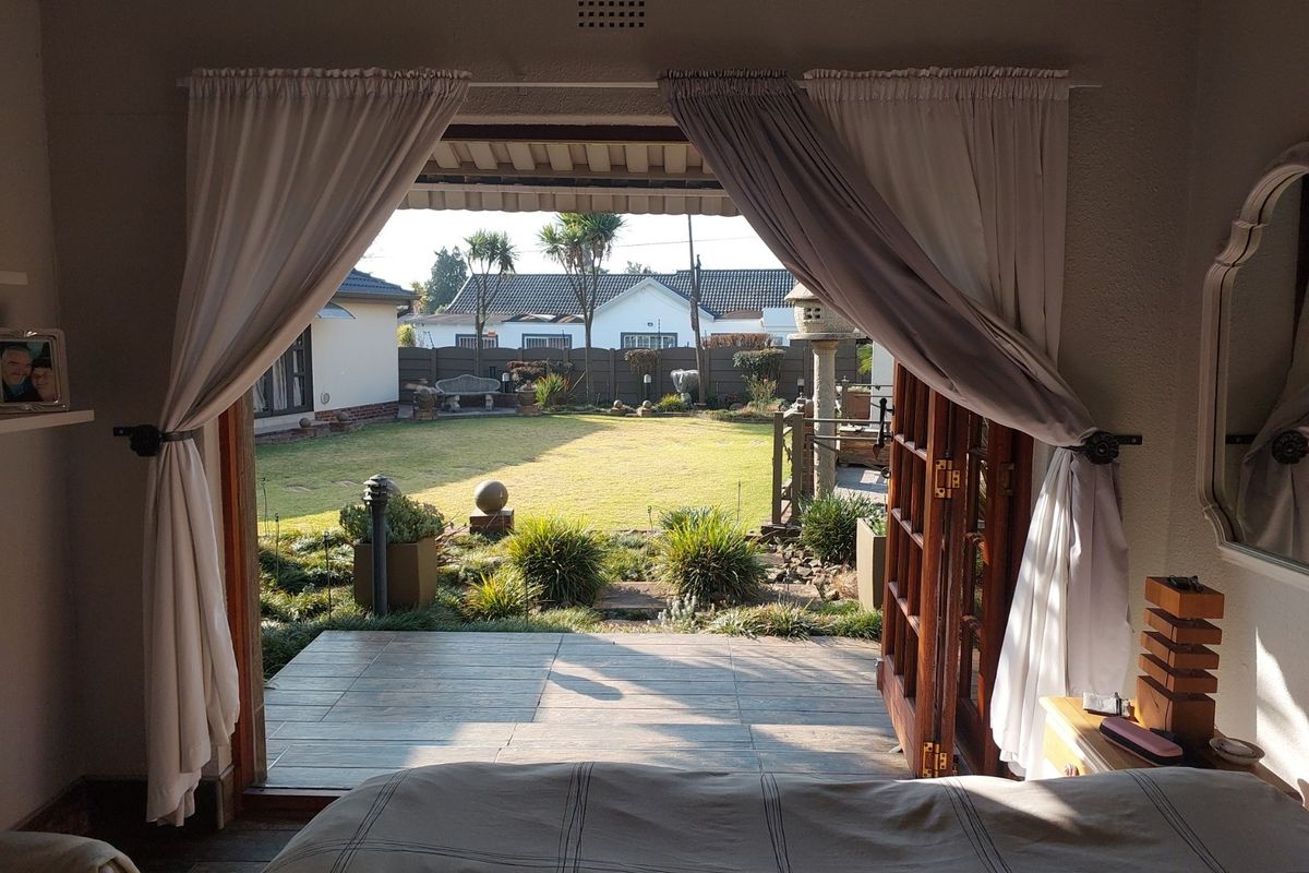 A bedroom featuring timber french doors that open onto a tiled patio and a well-maintained landscaped garden.
