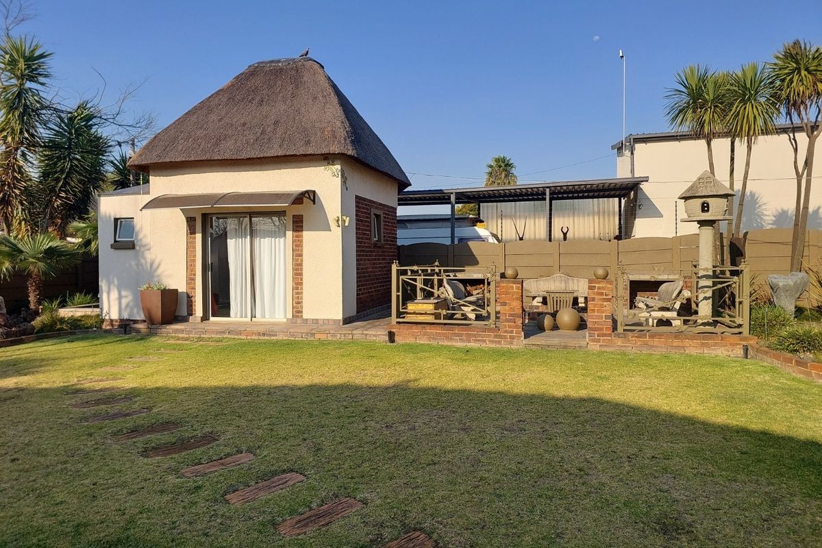Rear garden view featuring a detached outbuilding with a traditional thatch roof, sliding door access, and an adjacent paved patio area with brick walling.