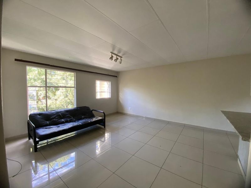 A spacious living area featuring neutral tiled flooring, track lighting, and large windows that provide ample natural light.