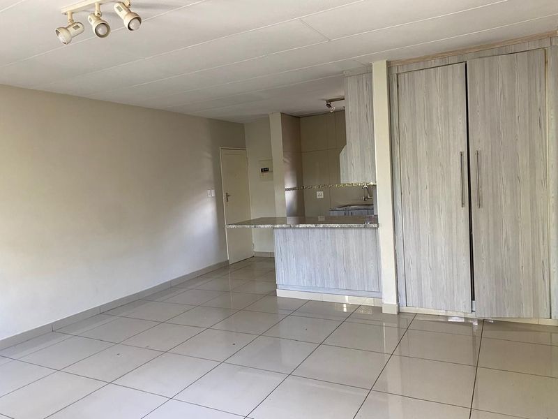 Open-plan living area featuring tiled flooring, built-in storage cupboards, and a functional kitchen with a breakfast bar counter.