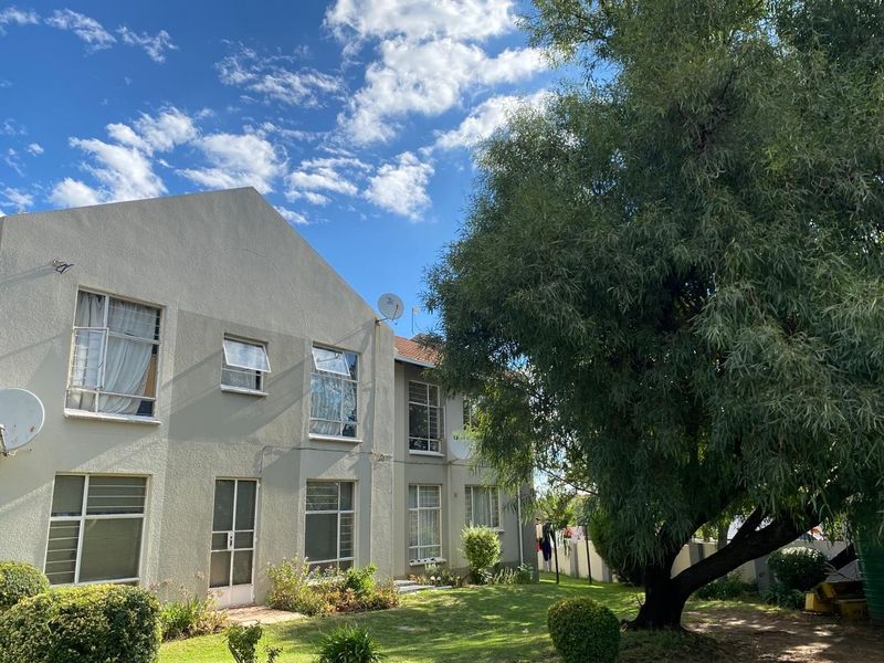 Rear view of a multi-story apartment building featuring a landscaped garden, mature trees, and exterior facade with security-fitted windows.