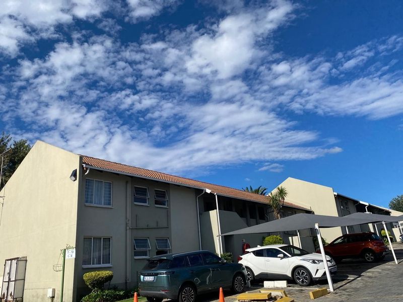 Exterior view of a multi-story apartment complex featuring a tiled roof, neutral facade, and dedicated covered parking bays for residents.