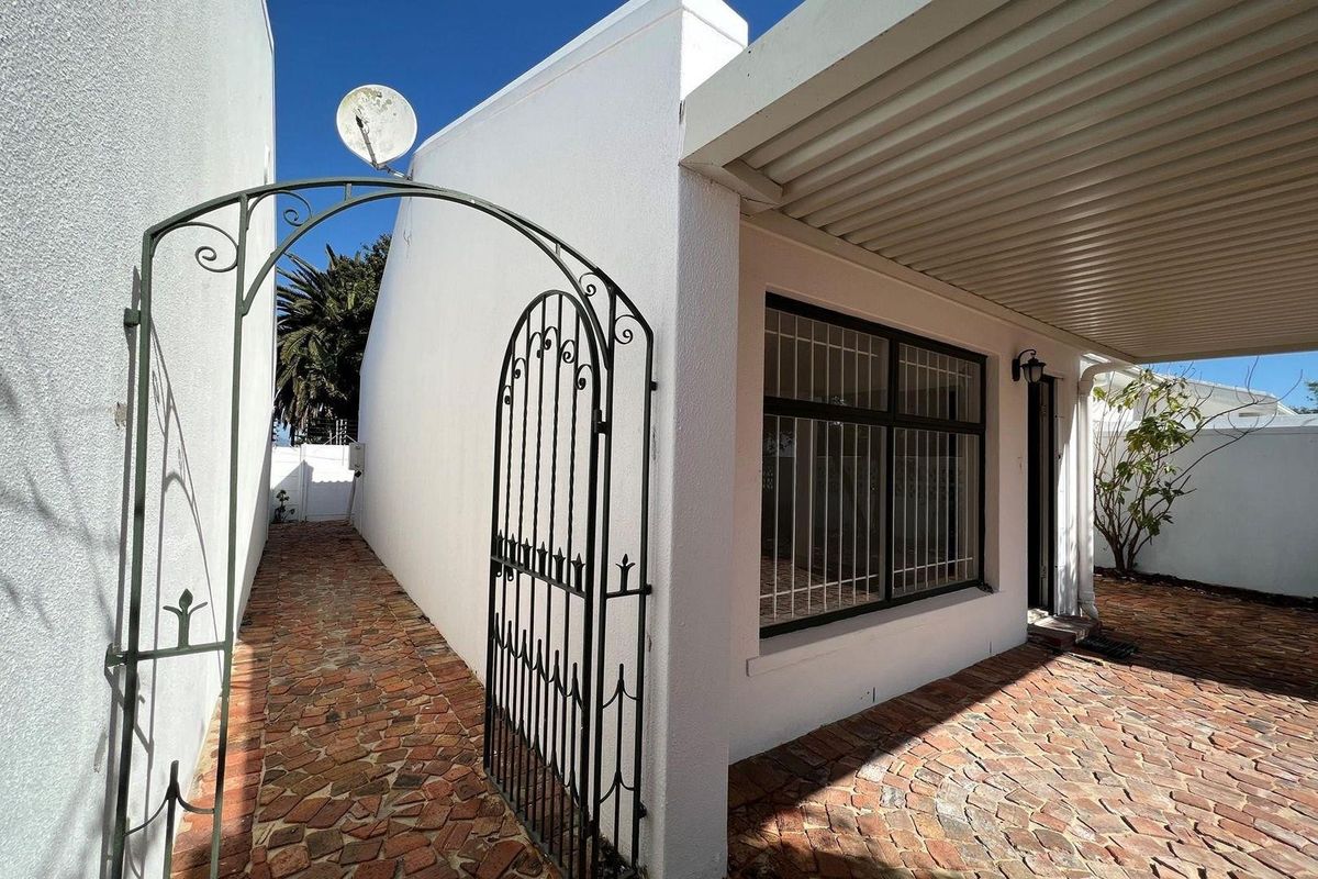 A well-maintained rear exterior area featuring a brick-paved patio, a covered walkway, and a secure wrought iron gate entrance.