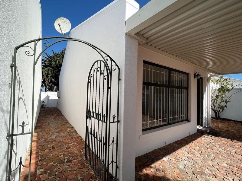A well-maintained rear exterior area featuring a brick-paved patio, a covered walkway, and a secure wrought iron gate entrance.