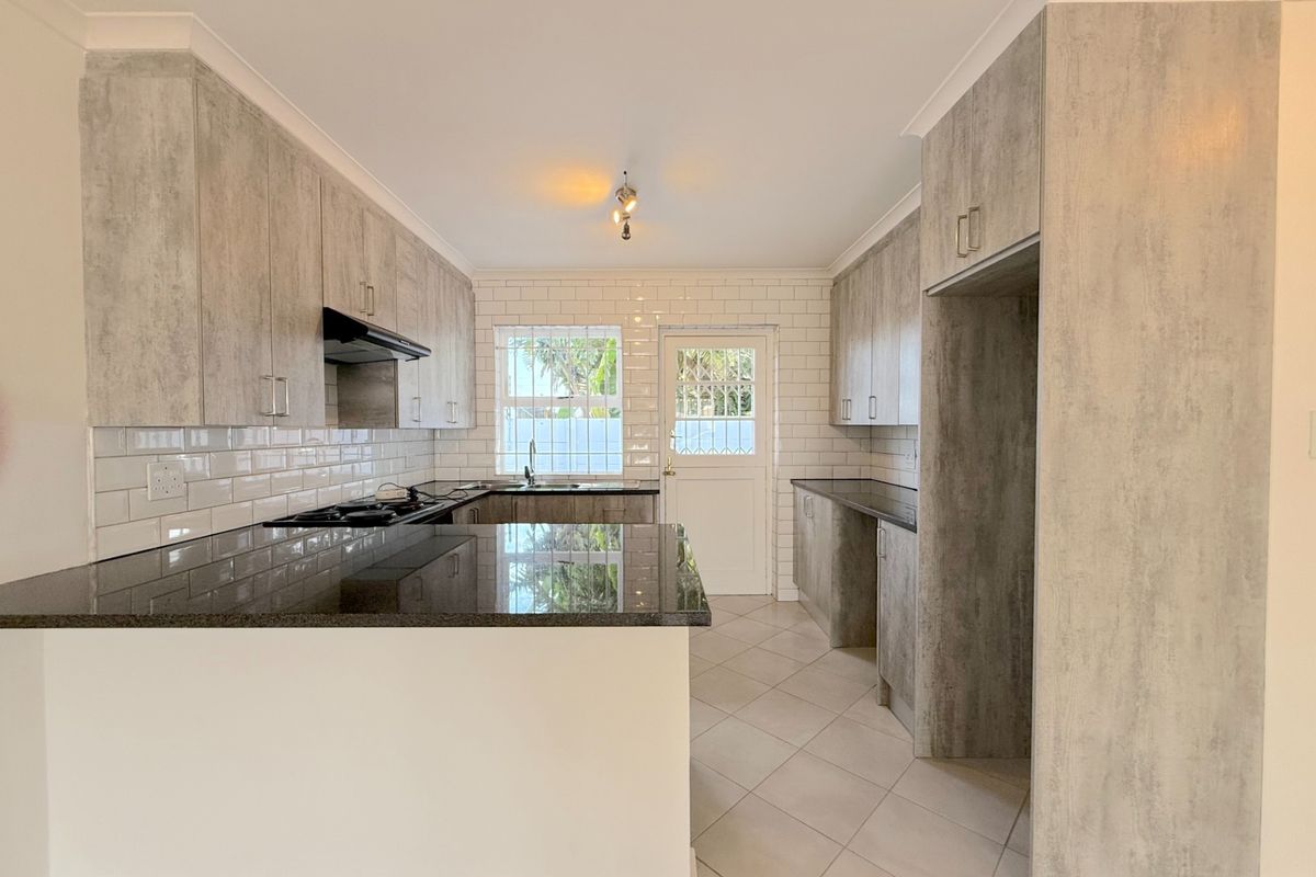 Modern kitchen featuring light wood-look cabinetry, dark granite countertops, subway tile backsplash, and tiled flooring with direct access to the exterior.