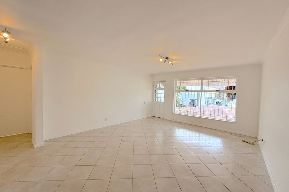 A bright, empty living room featuring neutral tiled flooring, security bars on the windows, and ceiling-mounted spotlights.