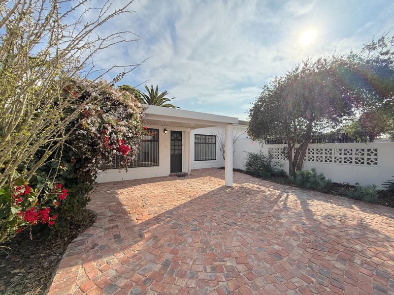 A well-maintained front entrance featuring a brick-paved driveway, a covered porch area, and decorative breeze block boundary walling.