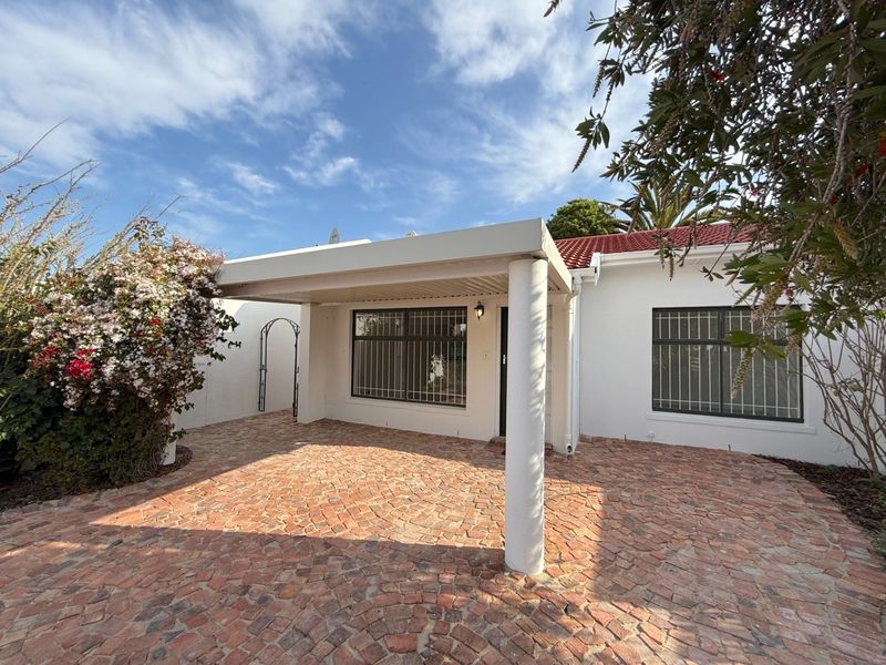 Front exterior view of the house featuring a covered patio area, brick paving, and secure window bars.
