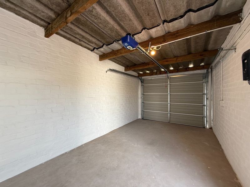A clean, empty single-car garage featuring painted brick walls, exposed timber ceiling beams, and an automated sectional garage door.