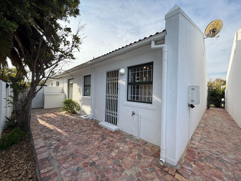 A rear exterior view of the property featuring a paved courtyard, security gate, and functional outdoor utility fixtures.