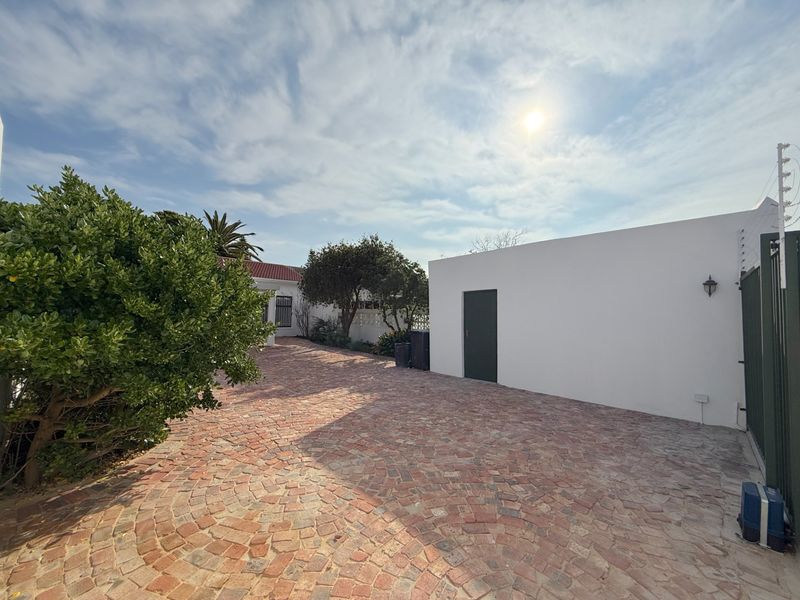 A view of the front exterior featuring a patterned brick paved driveway, boundary wall, and security electric fencing.