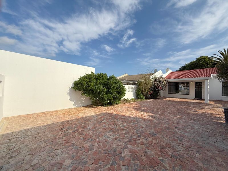 Front exterior view of the property featuring a spacious cobblestone driveway, boundary wall, and a tiled roof entrance.