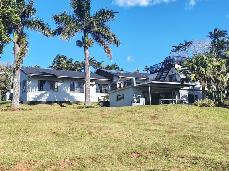 Rear view of the property featuring a spacious lawn, covered patio area, and an external staircase leading to an upper balcony.
