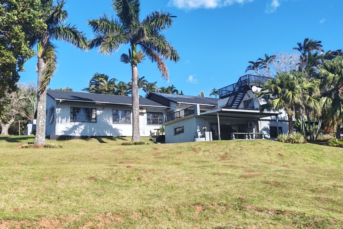 Rear view of the property featuring a spacious lawn, covered patio area, and an external staircase leading to an upper balcony.