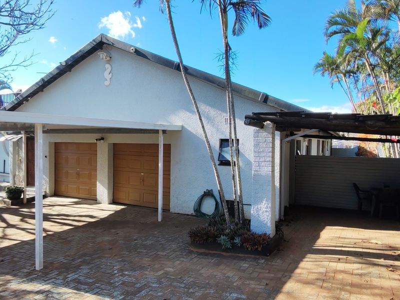 Front exterior view featuring a double garage, attached carport, paved driveway, and a timber pergola structure.