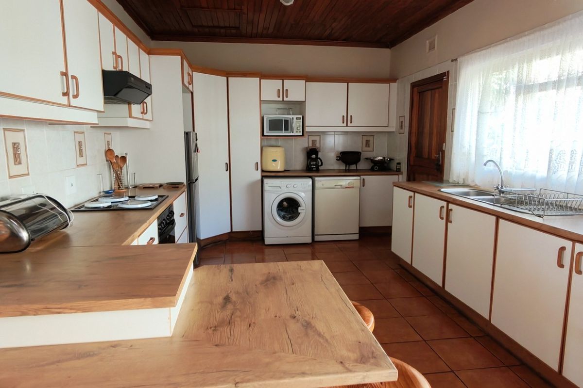 A functional kitchen featuring white cabinetry, wood-look laminate countertops, tiled flooring, and a timber ceiling, offering a classic, dated aesthetic.