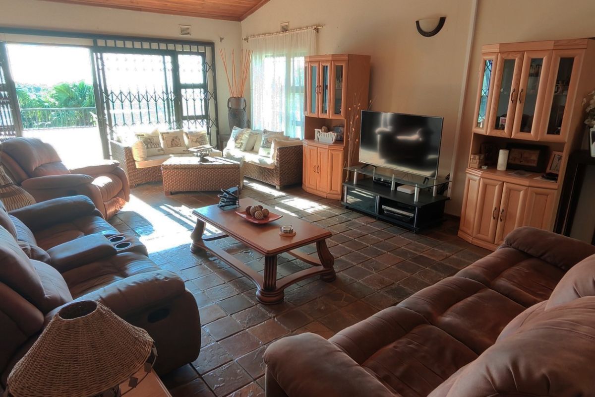 Spacious living room featuring rustic tiled flooring, a vaulted timber ceiling, and large sliding glass doors providing access to the outdoor area.