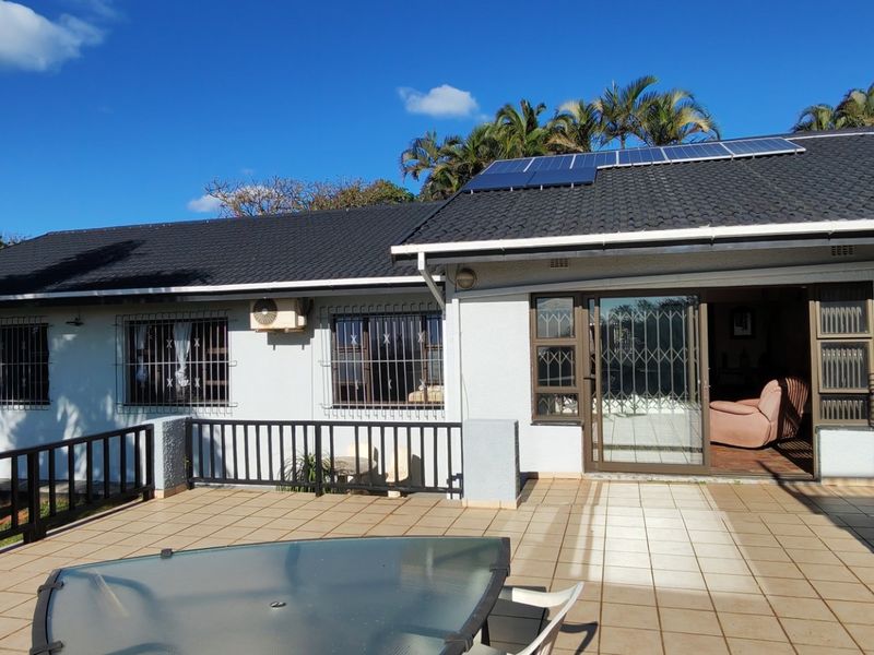 Spacious rear patio featuring tiled flooring and metal balustrades, providing access to the home through sliding glass doors with security bars.