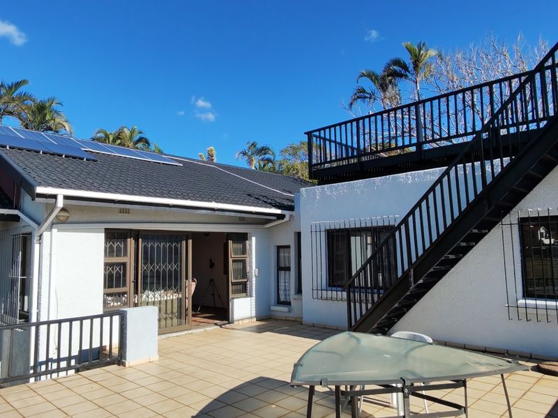Rear exterior view featuring a tiled patio, metal staircase leading to an upper deck, and roof-mounted solar panels.