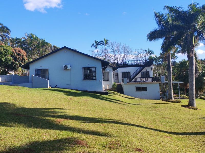 Rear view of the property featuring a large lawn, elevated balcony with external staircase access, and established garden surroundings.