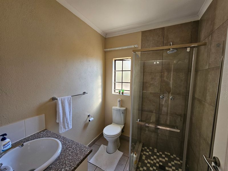A functional bathroom featuring a glass-enclosed shower, a vanity with a granite countertop, and a standard toilet.