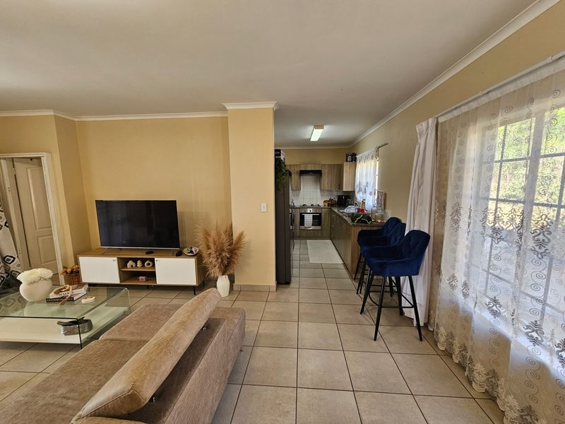 Open-plan living and kitchen area featuring tiled flooring, neutral wall tones, and a functional kitchen layout with built-in cabinetry and appliances.