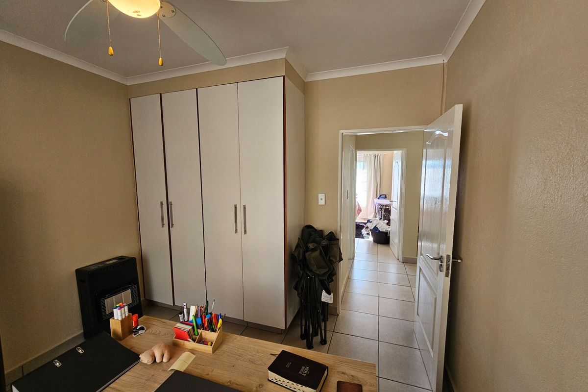 A bedroom featuring built-in wardrobes, a ceiling fan, and tiled flooring, with a doorway leading to an adjacent room.