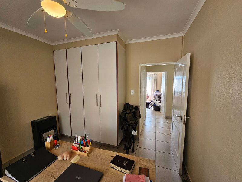 A bedroom featuring built-in wardrobes, a ceiling fan, and tiled flooring, with a doorway leading to an adjacent room.