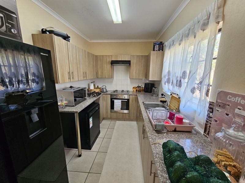 A functional kitchen featuring light wood-grain cabinetry, granite countertops, a built-in oven with gas hob, and tiled flooring.