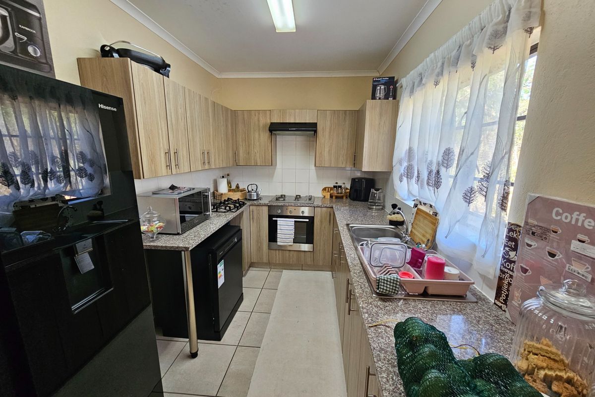 A functional kitchen featuring light wood-grain cabinetry, granite countertops, a built-in oven with gas hob, and tiled flooring.