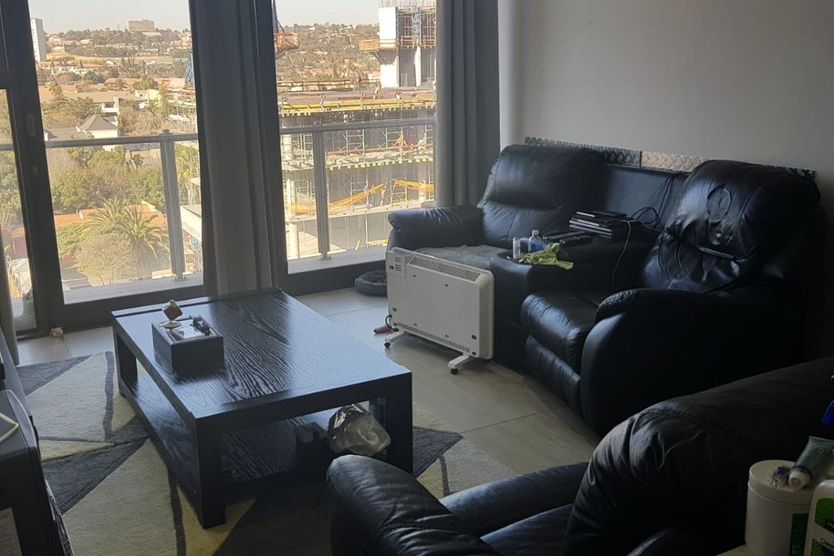 A living room featuring large floor-to-ceiling windows and a sliding door leading to a balcony, providing ample natural light and urban views.