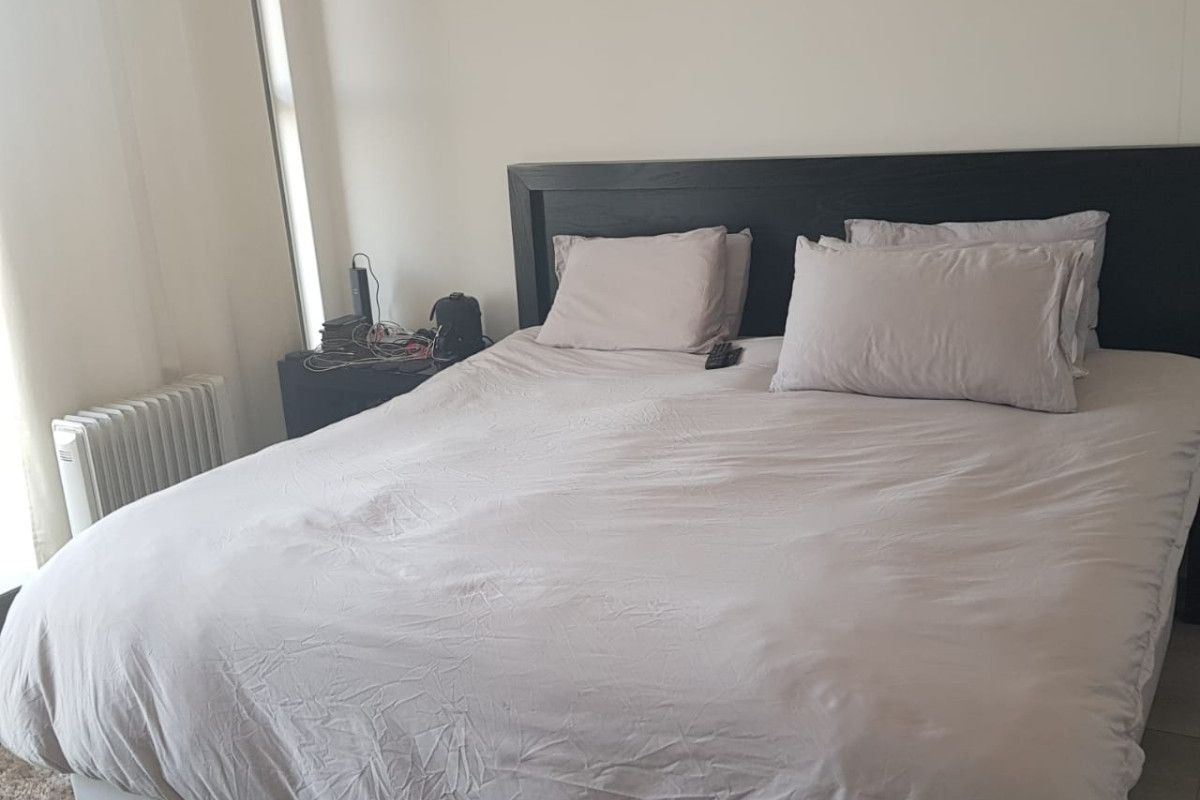 A bedroom featuring a built-in dark wood headboard and a wall-mounted radiator, providing a functional and neutral sleeping space.