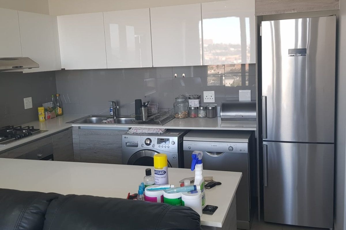 Modern kitchen featuring glossy white cabinetry, stone countertops, integrated stainless steel appliances, and a gas hob, offering a clean and functional cooking space.