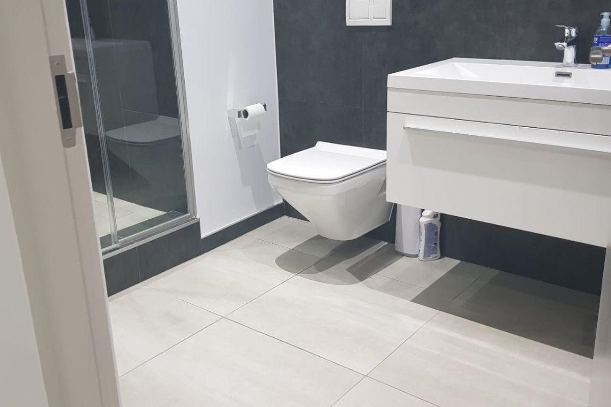 Modern bathroom featuring a wall-mounted toilet, sleek vanity basin, and a glass-enclosed shower with contemporary tiled finishes.
