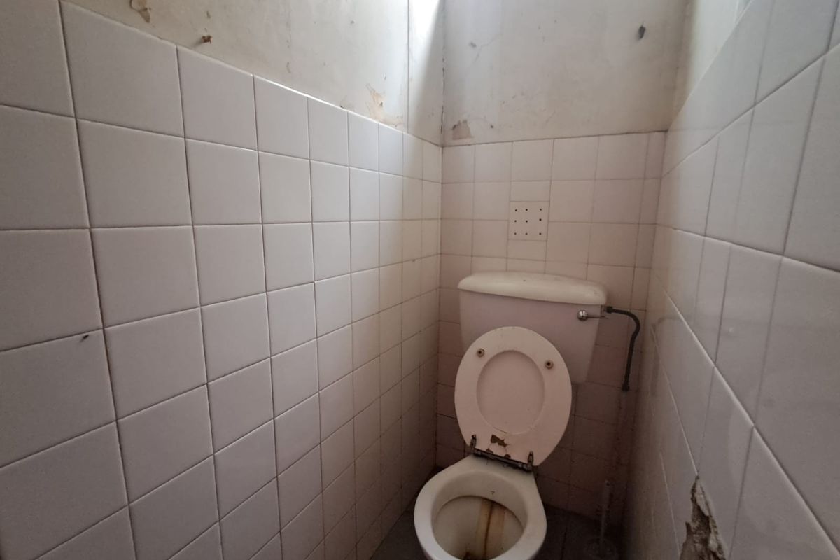 A small, dated bathroom featuring a standard toilet and tiled walls, currently requiring significant renovation and cosmetic repairs to improve its condition.
