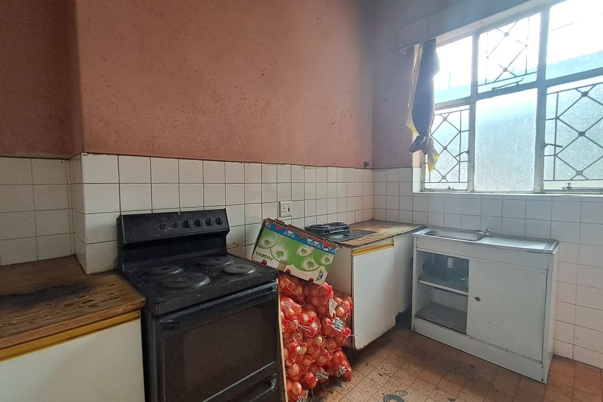 A dated kitchen featuring a freestanding stove, stainless steel sink, and tiled splashback, requiring significant renovation and modernization of finishes.
