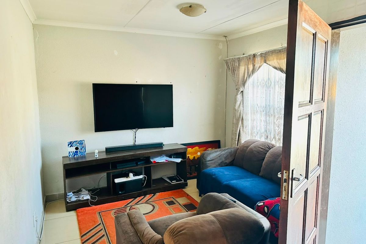 A compact living room featuring tiled flooring and a timber door, currently showing signs of wear on the wall surfaces.