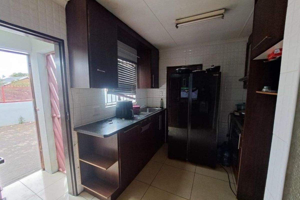 A functional kitchen featuring dark built-in cabinetry, tiled splashbacks, and direct access to the exterior through a side door.