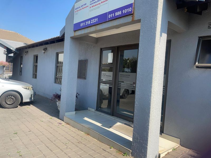 Front entrance of a commercial property featuring a paved driveway, aluminium glass door, and exterior signage.